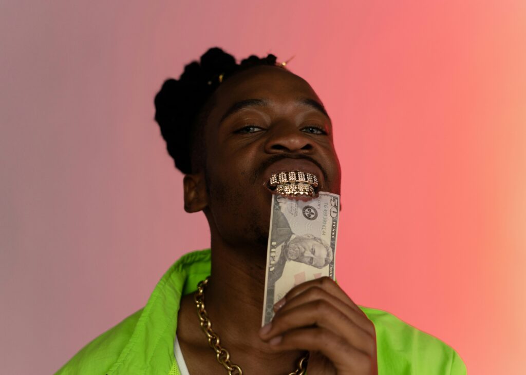 身穿螢光綠外套的男子嘴含美金鈔票與鑽石牙套，展現 trap music 的奢華形象