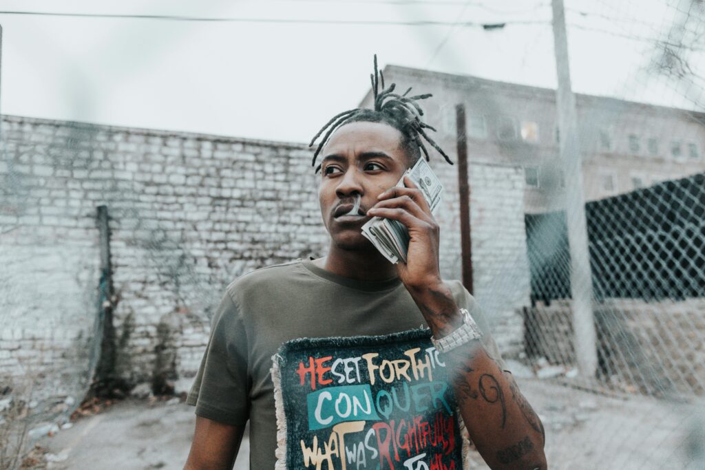 年輕男性在街頭拿著一疊鈔票模擬通話,展現 trap music 的街頭風格與自信態度