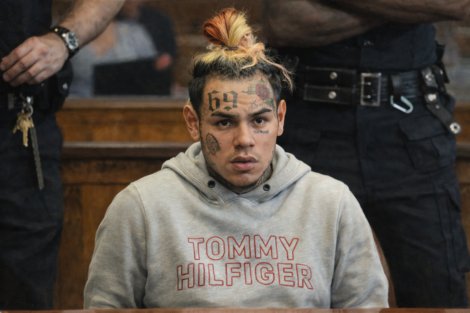 6ix9ine 坐在法庭內,額頭「69」刺青與臉部紋身清晰可見,身穿灰色連帽上衣,神情嚴肅