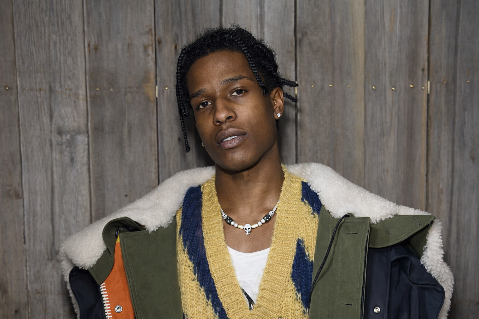 A$AP Rocky 身穿層次穿搭外套與針織背心的時尚形象照