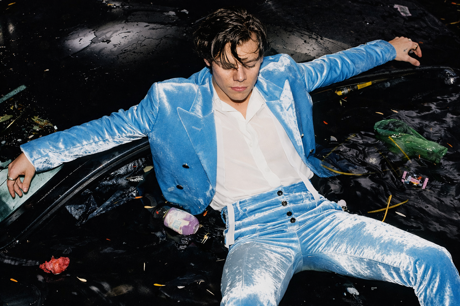Harry Styles 身穿藍色絲絨西裝躺臥於黑色水面中,呈現藝術感十足的時尚形象照