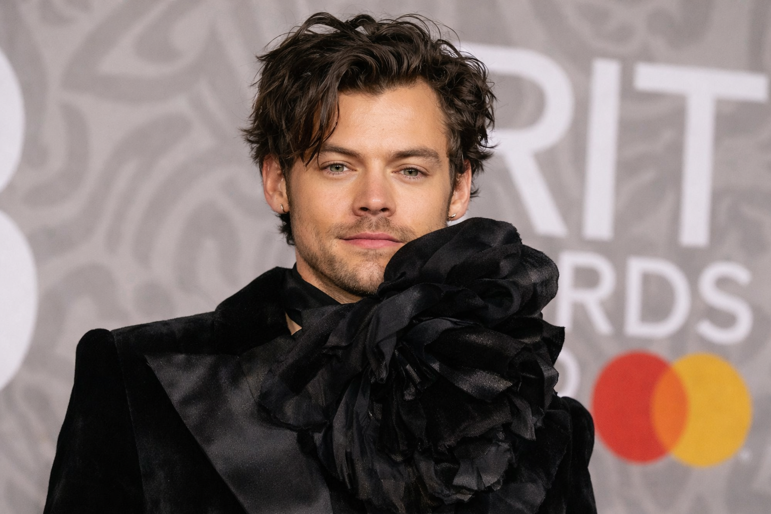 Harry Styles 身穿黑色高訂西裝與立體花飾圍巾出席頒獎典禮紅毯,展現個人時尚風格與藝術氣質